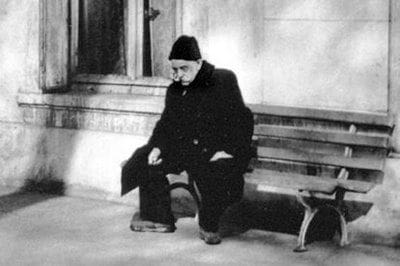 A man sitting on the bench in front of a building.