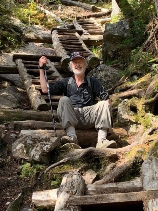 Here's an 8-word alt tag for the image: Hiker resting on log steps in mountain trail.